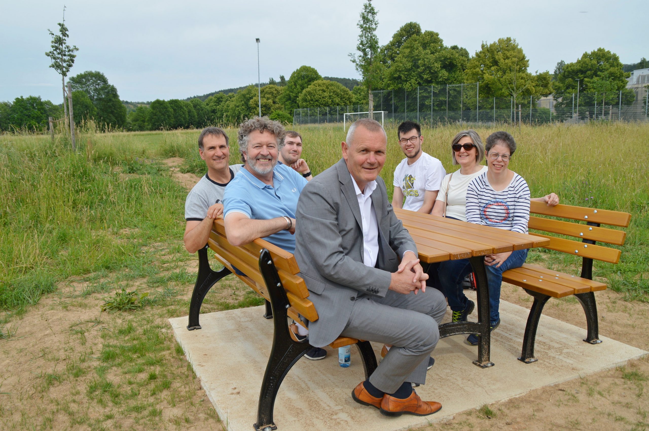 2026-06 Sitzgruppe-1 Gemütliches Probesitzen an der neu aufgestellten Sitzgruppe am Marktheidenfelder Südring: (von links) Gruppenleiter Entwicklung bei Cummins Andreas Lannig, Lebenshilfe-Geschäftsführer Rüdiger Hohe, David Kasamas, Erster Bürgermeister Thomas Stamm, Jonah Kuhn, Betreuerin Manuela Harth und Alessandra Schnarr. Foto: Marcus Meier